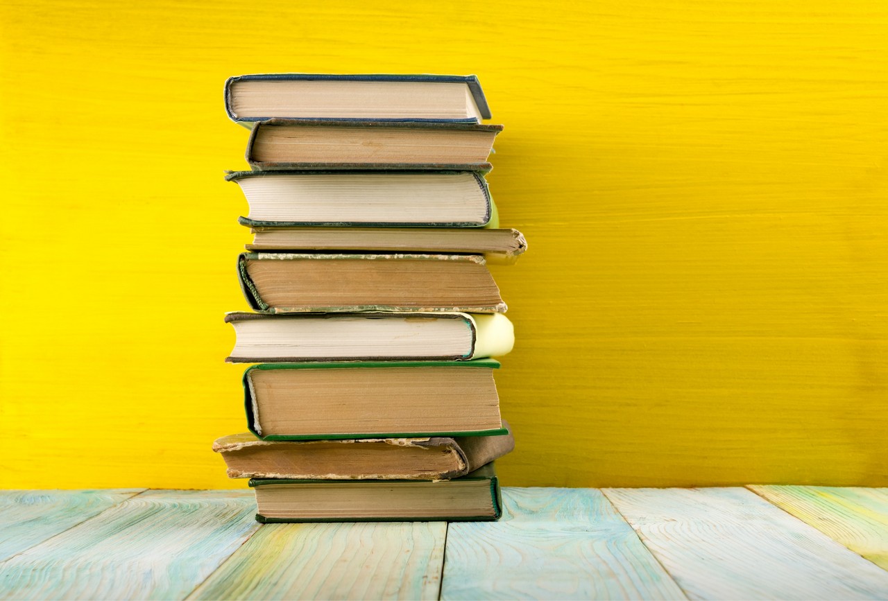 Colorful composition with vintage old hardback books, diary on wooden deck table and yellow background. Books stacking. Back to school. Copy Space. Education background